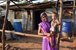Hymyilevä nainen lapsi sylissään hökkelin edustalla Intiassa
