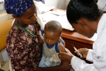 Nainen antaa rokotetta toisen naisen sylissä olevalle vauvalle.