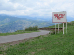 Vuoristomaisema, tie ja armenialaisilla aakkosilla varustettu tienvarsikyltti.