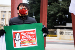 Maskilla suojautunut mies pitää kädessään kylttiä, jossa lukee We stand with the people of Myanmar: never again to military rule.