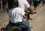 Lapsi kypärä päässä aikuisen takana mopon tai moottoripyörän kyydissä.