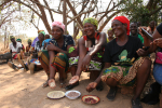 Hymyileviä naisia edessään kuivattuja papuja lautasilla Sambian maaseudulla