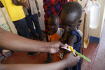 Aikuinen mittaa lapsen käsivarren paksuutta Keniassa