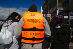 Mielenosoittaja, jonka yllä pelastusliivi ja selässä teksti No Borders No Nation