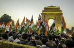 Miehiä Intian lippujen kera mielenosoituksessa, taustalla Delhin India Gate -monumentti