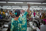 Bangladeshilainen vaatetyöläinen heiluttaa muille vaatetyöntekijöille tehtaassa