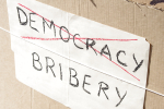 Kyltti, jossa lukee bribery - yläpuolella rastittu sana democracy