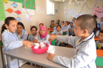 Lapsia koululuokassa opiskelemassa haarukoiden ja muovimukien avulla