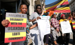 Mielenosoittajia kylttien ja Ugandan lippujen kanssa