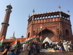Minareetti ja moskeija, jonka edustalla ihmisiä ja Intian lippuja