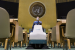 Mies ajaa tuolien välistä siivouskoneella, taustalla YK:n logo.