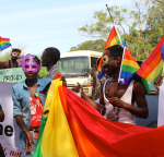 Kaksi ugandalaista pitää kädessä pridelippua, kasvoillaan karnevaalinaamiot.