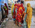 Intialaisia naisia kadulla selin kameraan. Naisilla on värikkäät huivit päässä.