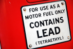Punaisella pohjalla valkoinen kyltti, jossa lukee mustalla tekstillä "for use as a motor fuel only contains lead (tetraethyl)".