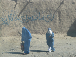 Kaksi naista burkhat päällä, taustalla tekstiä kallioon maalattuna.