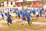 Kymmeniä lapsia juoksee koulurakennuksen pihalla.